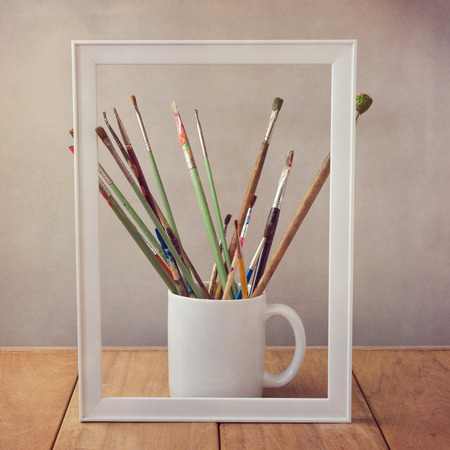 Artist painting brushes on wooden table with picture frameの写真素材