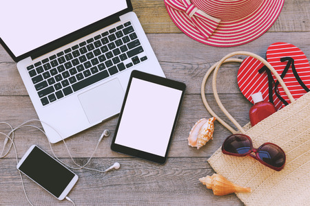 Laptop, digital tablet and smart phone with beach items over wooden background. View from aboveの写真素材