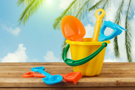 Children bucket and spade on wooden table over palm tree backgroundの写真素材