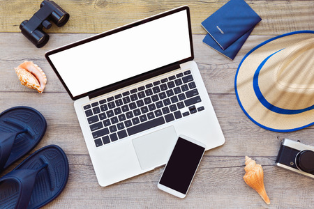 Laptop computer and smart phone with male summer holiday accessories on wooden boardの写真素材