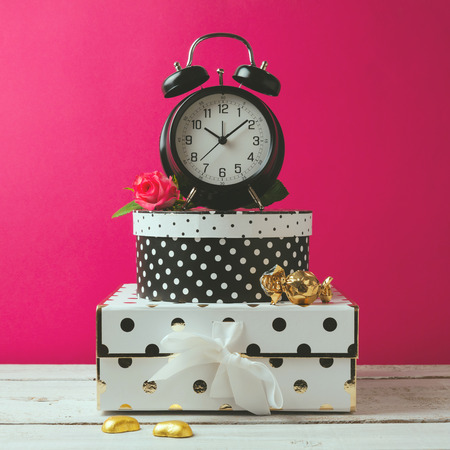 Alarm clock with polka dots boxes over pink modern background. Glamour feminine objectsの写真素材