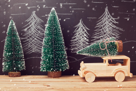 Christmas celebration concept with christmas tree on toy car on wooden table over chalkboard backgroundの写真素材