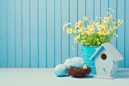 Easter holiday decoration with daisy flowers, eggs and birdhouse over blue backgroundの写真素材