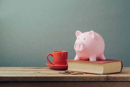 Piggy bank on wooden table with coffee cup and book. Saving money, budget planning concept.の写真素材