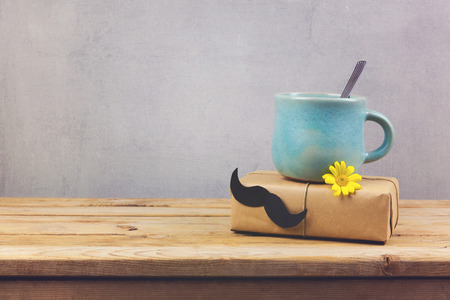 Coffee cup and gift box with paper mustache on wooden table. Father's day holiday conceptの写真素材