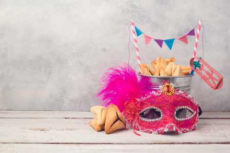 Purim holiday concept with hamantaschen cookies or hamans ears in bucket and carnival mask over rustic backgroundの写真素材