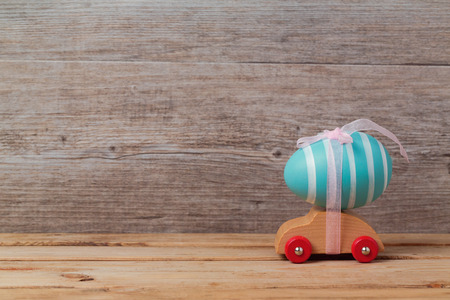 Easter holiday concept with egg on toy car over wooden backgroundの写真素材
