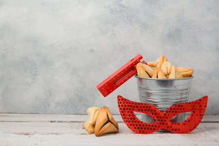 Purim holiday concept with hamantaschen cookies or hamans ears in bucket and carnival mask over rustic backgroundの写真素材