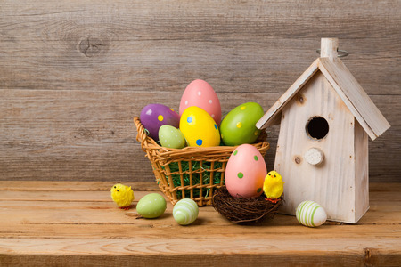 Easter holiday concept with eggs basket and bird house over wooden backgroundの写真素材