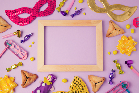 Purim holiday concept with wooden frame, carnival mask and hamans ears cookies on purple background. Top view from above. Flat layの写真素材