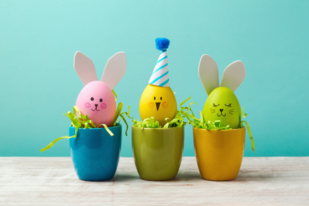 Easter holiday concept with cute handmade eggs, bunny, chicks and party hats in cup on wooden tableの写真素材