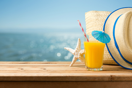 Summer holiday vacation concept with orange juice, hat and bag over sea beach background