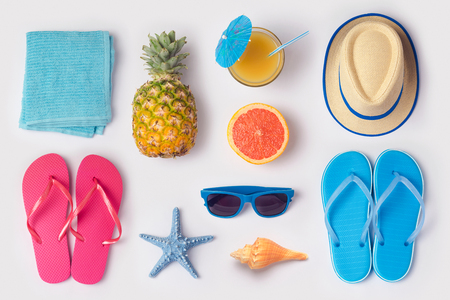 Tropical summer vacation concept with pineapple, juice and flip flops organized on white background. View from above. Flat lay