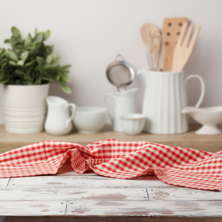 Empty wooden table with red checked tablecloth over kitchen shelf backgroundの写真素材