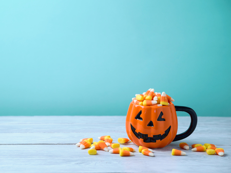 Halloween celebration concept with candy corn and jack o lantern cup on wooden table.