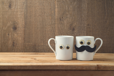 Happy Fathers day concept with two coffee cups as father and son funny characters over wooden backgroundの写真素材