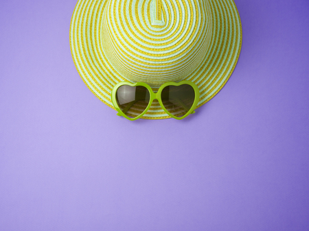 Minimal summer concept. Yellow hat and sunglasses over violet background. View from aboveの写真素材