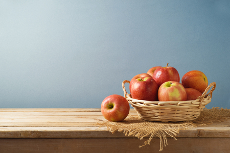 Red apples in basket on wooden kitchen table backgroundの写真素材