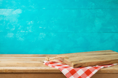 Empty wooden cutting board on kitchen table with tablecloth over blue background