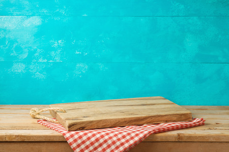 Empty wooden cutting board on kitchen table with tablecloth over blue backgroundの写真素材