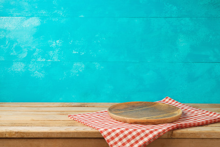 Empty wooden plate or tray on kitchen table with tablecloth over blue background