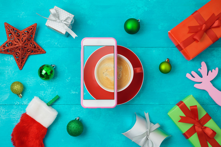 Christmas holiday creative concept with coffee cup, smart phone, gift boxes and decorations on wooden table. Top view from above.の写真素材