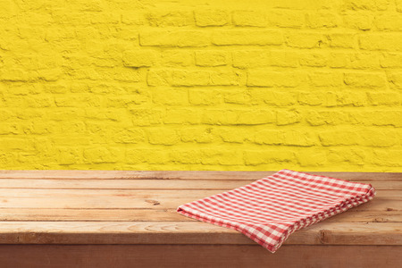 Empty wooden table with tablecloth over yellow brick stone wall background.