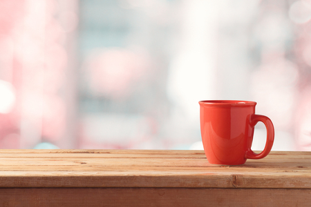 Red coffee or tea cup  on wooden table over abstract bokeh background with copy space. Mock up or key visual design layoutの写真素材