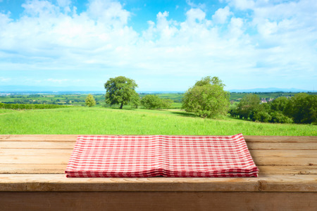 Empty wooden table with tablecloth over summer meadow background