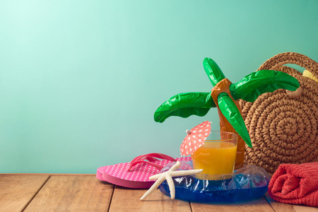 Summer vacation background with orange juice, beach accessories and pool float on wooden table