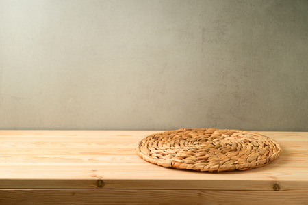 Empty wooden table with wicker round placemat over rustic wall backgroundの写真素材