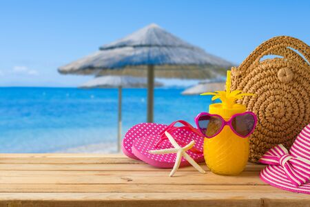 Summer holiday vacation concept with pineapple juice, beach fashion bag and flip flops on wooden...