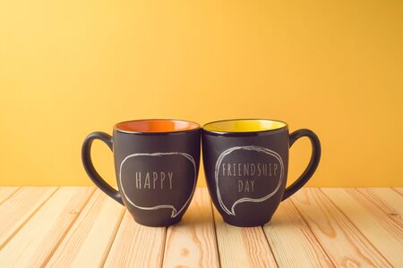 Chalkboard coffee mugs on wooden table with happy friendship day text. Friendship day conceptの写真素材