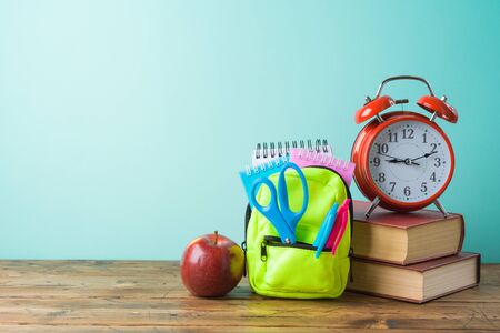 Back to school background with small backpack, books and alarm clock on wooden table