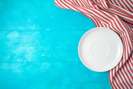 White empty plate and red striped tablecloth on blue wooden background. Top view from above