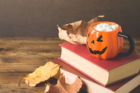 Halloween holiday concept with hot chocolate cup, books and autumn leavesの写真素材