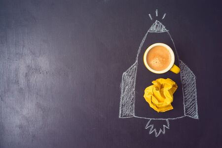 Business concept of brainstorming, idea or start up with rocket sketch, coffee cup and crumpled paper over chalkboard background.の写真素材