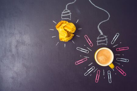 Business concept of brainstorming, idea or start up with light bulb sketch, coffee cup and crumpled paper over chalkboard background.の写真素材