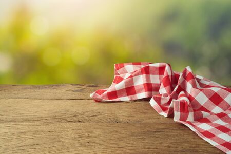 Empty wooden table with red checked tablecloth over green bokeh background.の写真素材