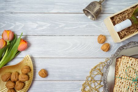 Jewish holiday Passover background with matzo, seder plate, wine and tulip flowers on wooden table....