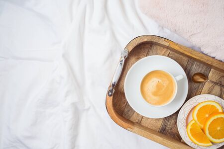 Coffee cup and fresh oranges on wooden tray on morning bed background. Stay at home concept. Top view from aboveの写真素材