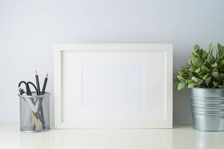 White frame mock up with pencils and home plant decor