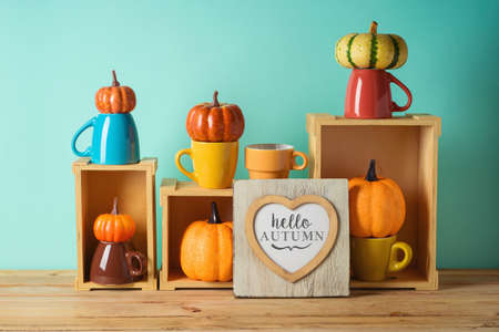 Hello Autumn concept with heart shape photo frame and pumpkin decor on wooden table over blue...