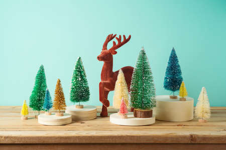 Christmas decor concept with colorful Christmas trees and reindeer on wooden table over blue...
