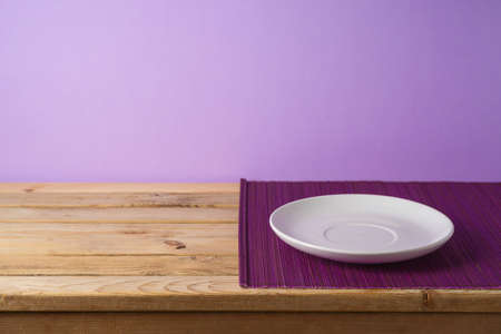 Empty white plate with bamboo mat on wooden table over purple background. Kitchen or restaurant counter mockup for designの写真素材