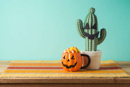 Halloween holiday concept with jack o lantern pumpkin cup, candy corn and cactus on wooden table over blue  backgroundの写真素材