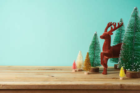 Christmas decor concept with colorful Christmas trees and reindeer on wooden table over blue background. Winter season and happy holidays greeting card.の写真素材