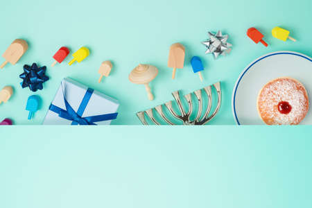 Jewish holiday Hanukkah concept with menorah, sufganiyah, gift box and spinning top over blue...