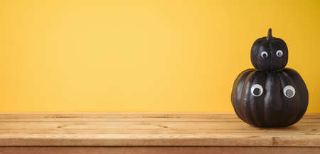 Empty wooden table with Halloween black pumpkin decor over yellow backgroundの写真素材