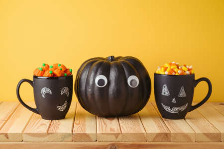 Halloween holiday creative concept with black pumpkin, chalkboard coffee mugs and candy corn on...